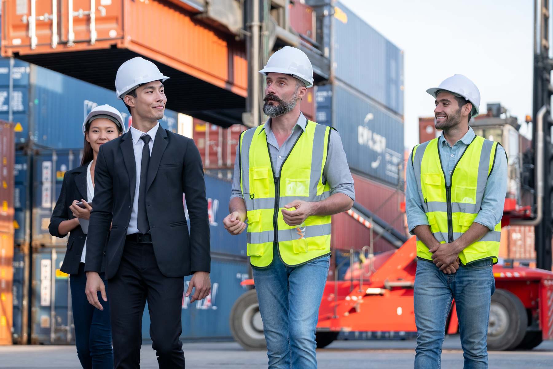Logistics consulting team walking through a shipping yard, discussing operations with professionals in safety gear.