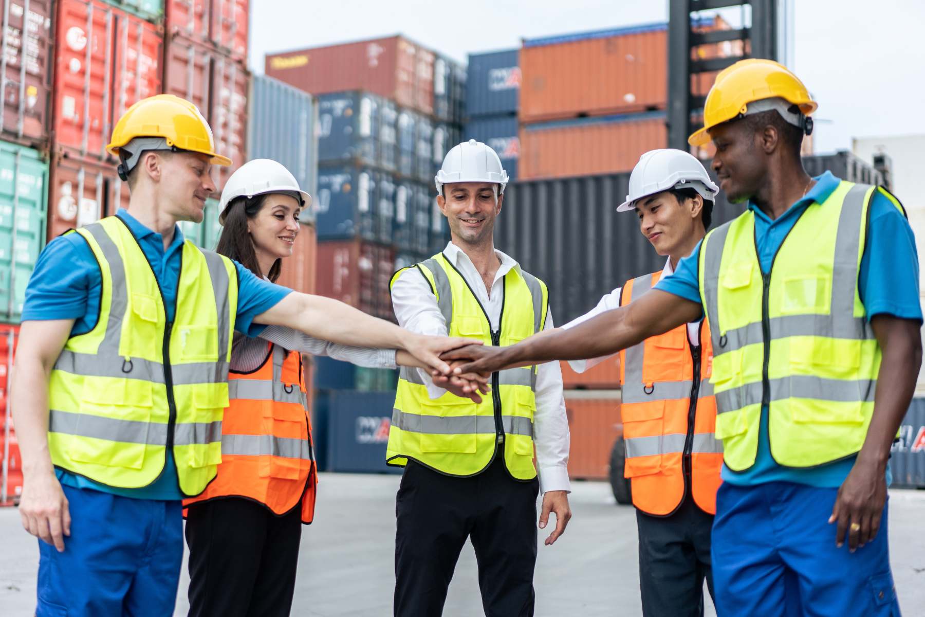 Logistics team collaborating and celebrating success with a group huddle in front of shipping containers, showcasing teamwork in operations.